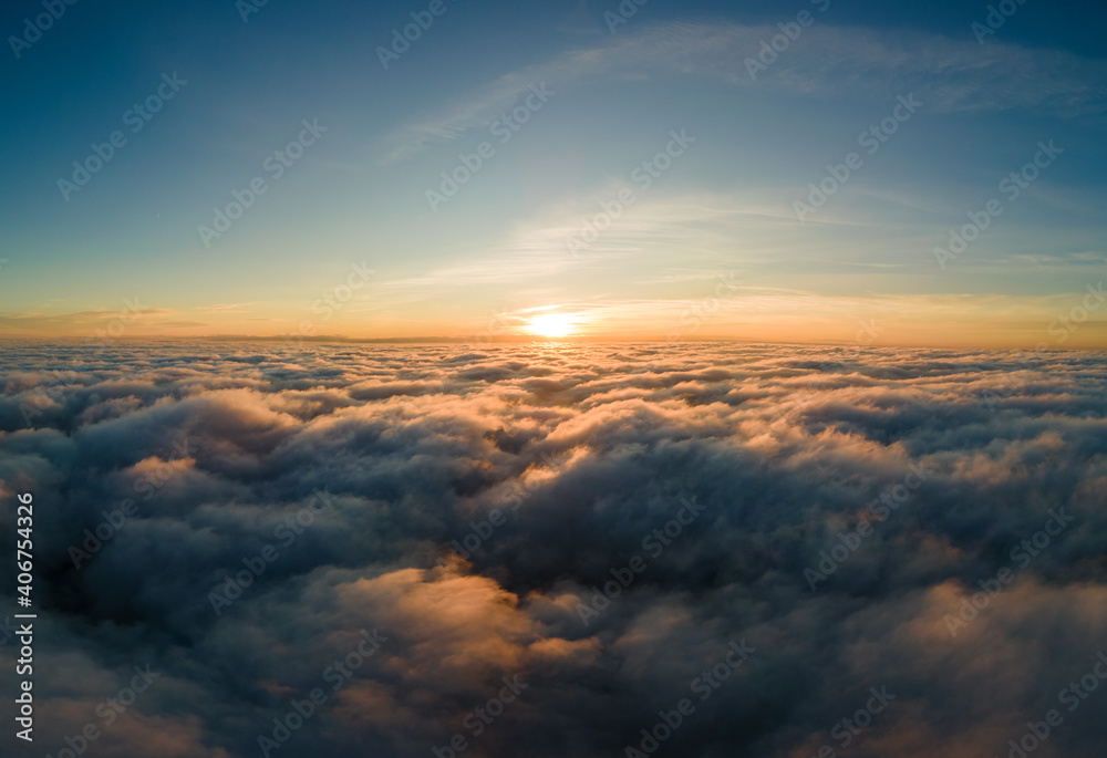 Aerial view of bright yellow sunset over white dense clouds with blue sky overhead. Aerial view of bright yellow sunset over white dense clouds with blue sky overhead.