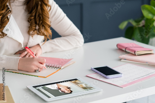 Online education. Video call. Distance learning. Virtual class. Female student watching listening teacher digital lesson on tablet screen at modern white workplace with pink office supplies.