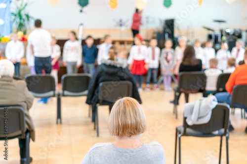 Parents at the performance of children in kindergarten or school. Children on stage. Many parents are watching the kids performance in the hall during Chistmas holiday, blurry