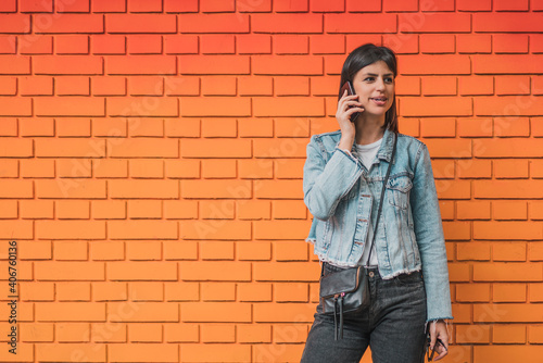 Attractive young woman posing and talking on mobile phone on a background of a red colorful brick wall. Empty space for text o design.