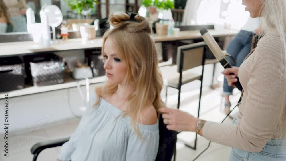 Close-up view of stylist hairdresser making hairstyle using curling tongs for long hair of unrecognizable woman in beauty salon. Concept of beauty and fashion Close-up view of stylist hairdresser making hairstyle using curling tongs for long hair of unrecognizable woman in beauty salon. Concept of beauty and fashion