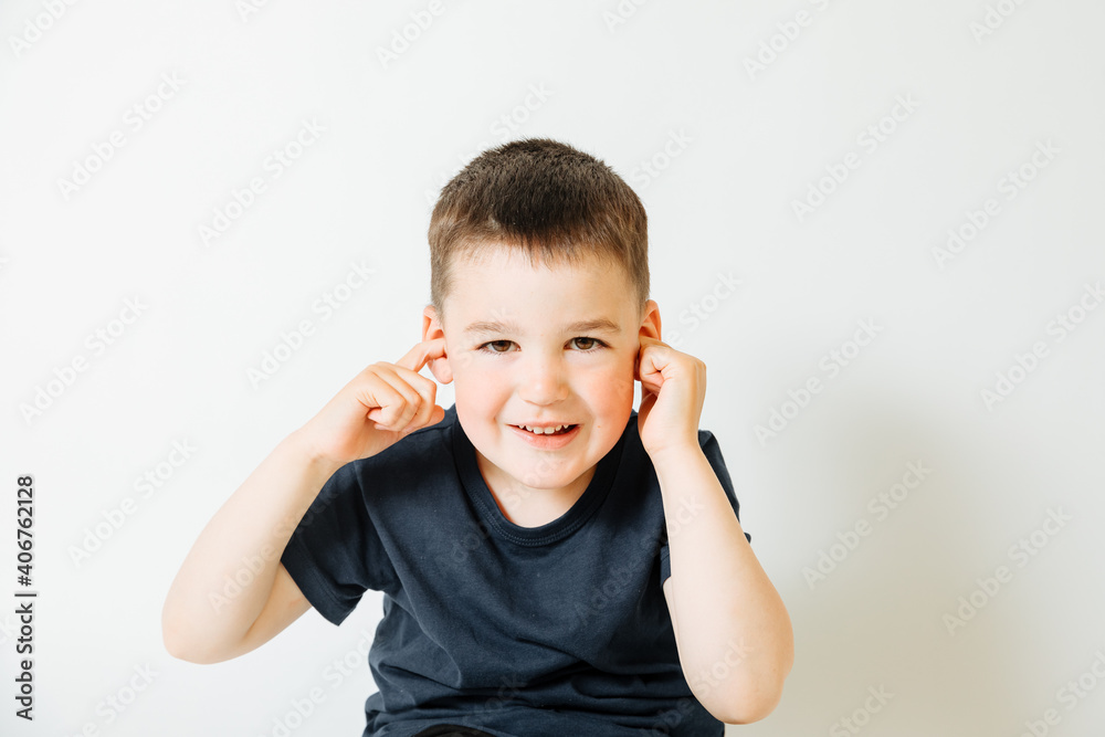 little boy on white background smiles and covers one ear. raising children little boy on white background smiles and covers one ear. raising children