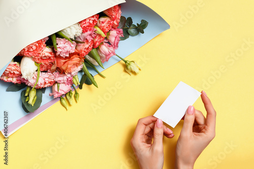 Close-up of female hands holding a card with a message and a bouquet of pink roses on a yellow background.