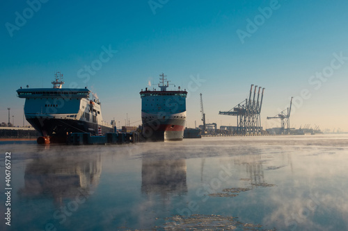 Huge see cargo boats in port in Klaipeda, Lithuania. Bay view from a ferry in frosty cold January winter sunny day. Am ice on smoke fog on the water photo