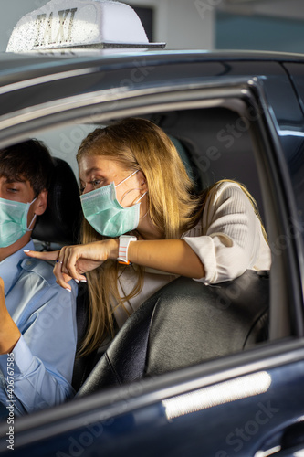 Caucasian young woman wearing protective face mask traveling with taxi and man driver. 