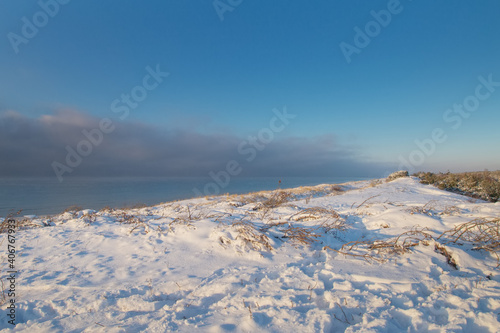 Snow Curonian Spit dunes in January winter sunny day. Blue sky and sea, no people on the beach, calm and beautiful view. Near Klaipeda city in Lithuania