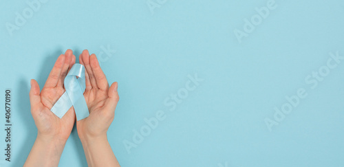  Woman hands holding blue ribbon, as a symbol of diabetes over blue pastel background.
