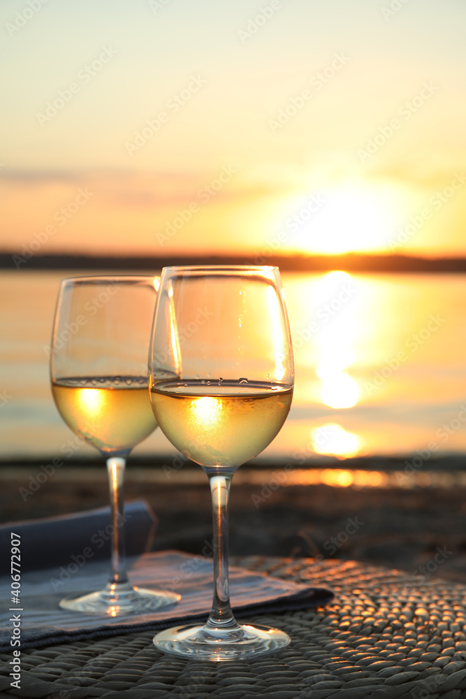 Glasses of delicious wine on riverside at sunset