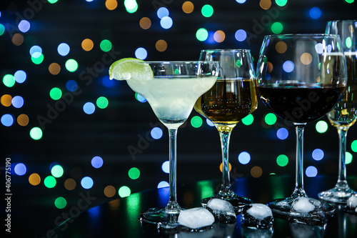 Many different alcoholic drinks on table against dark background with blurred lights