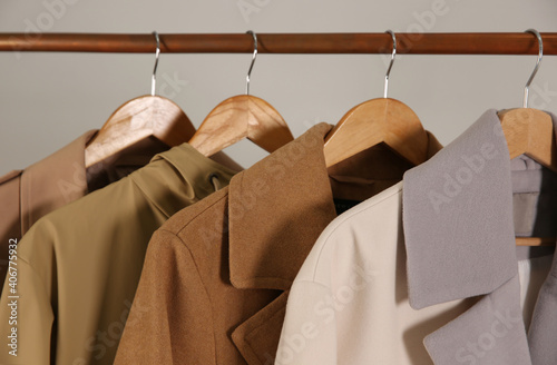 Different warm coats on rack against light grey background, closeup photo