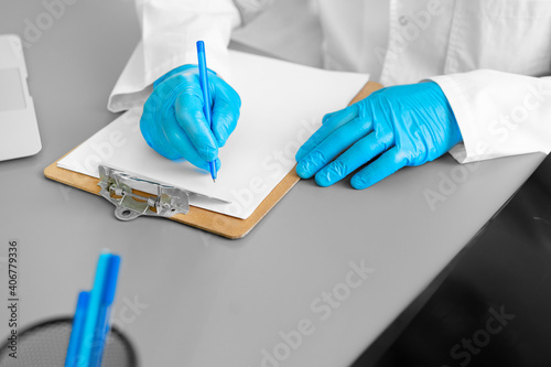 Unrecognizable doctor in gloves making notes while sitting at his working table