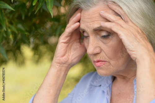 Sad senior woman with headache in park