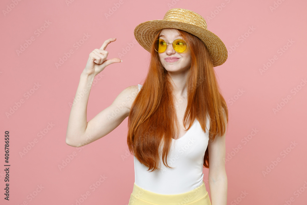 Young redhead cute displeased woman 20s ginger long hair wear straw hat glasses summer clothes gesturing demonstrating size with workspace isolated on pastel pink color background studio portrait. Young redhead cute displeased woman 20s ginger long hair wear straw hat glasses summer clothes gesturing demonstrating size with workspace isolated on pastel pink color background studio portrait.