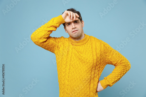 Young unshaved tired exhausted displesed troubled sad man 20s wear casual knitted cozy yellow fashionable sweater put hand on forehead with headache isolated on blue color background studio portrait. photo