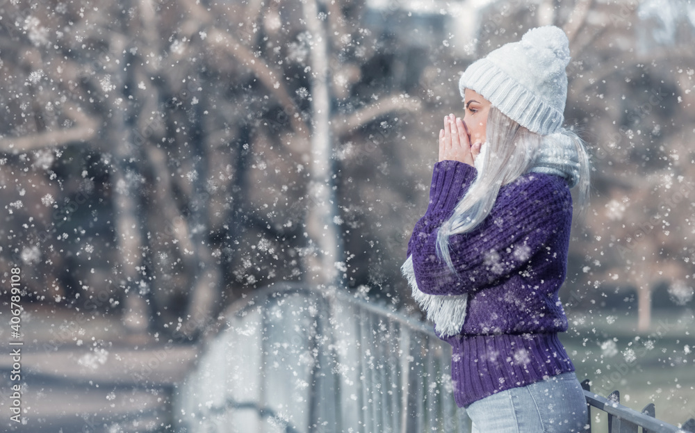 Side view young woman warming her hands, wears warm clothing on snowing winter day outdoors. Cute girl feeling cold. Winter concept. Side view young woman warming her hands, wears warm clothing on snowing winter day outdoors. Cute girl feeling cold. Winter concept.