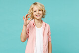 Smiling funny little curly kid boy 10s in pastel pink shirt showing ok okay gesture looking camera isolated on blue turquoise color background children studio portrait. Childhood lifestyle concept.