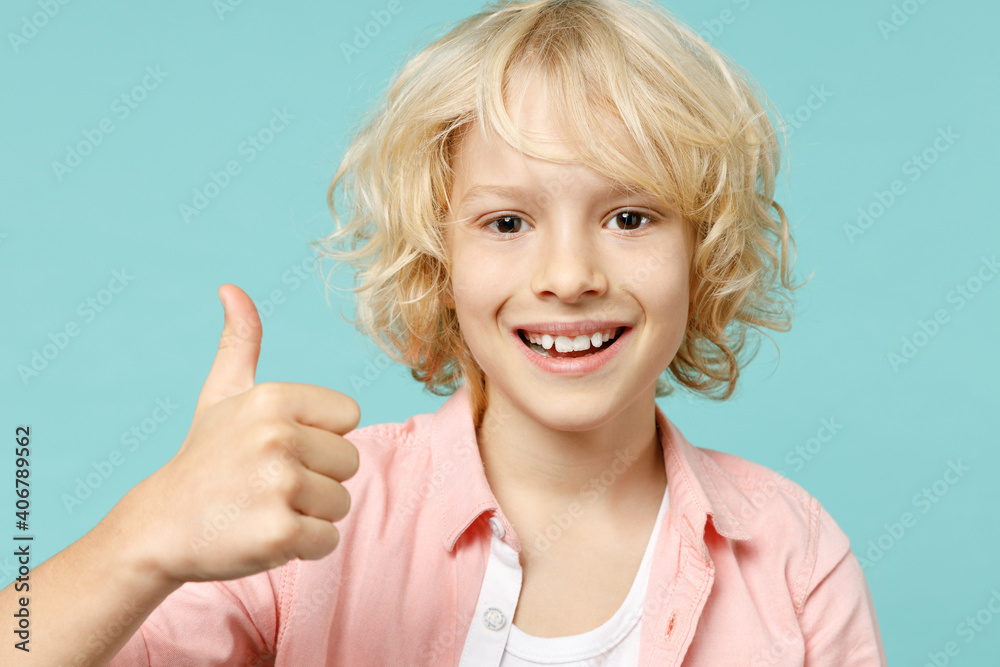 Cheerful little curly kid boy 10s years old wearing pastel pink shirt showing thumb up looking camera isolated on blue turquoise color background children studio portrait. Childhood lifestyle concept. Cheerful little curly kid boy 10s years old wearing pastel pink shirt showing thumb up looking camera isolated on blue turquoise color background children studio portrait. Childhood lifestyle concept.