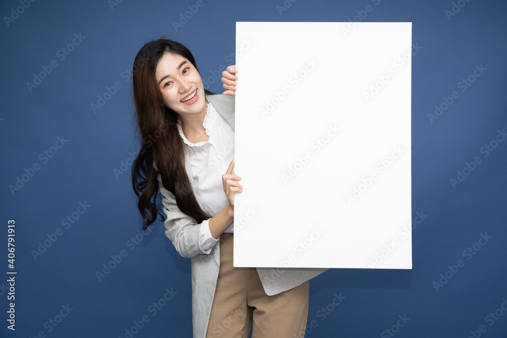 Asian business woman showing and holding blank white billboard isolated on deep blue background Asian business woman showing and holding blank white billboard isolated on deep blue background