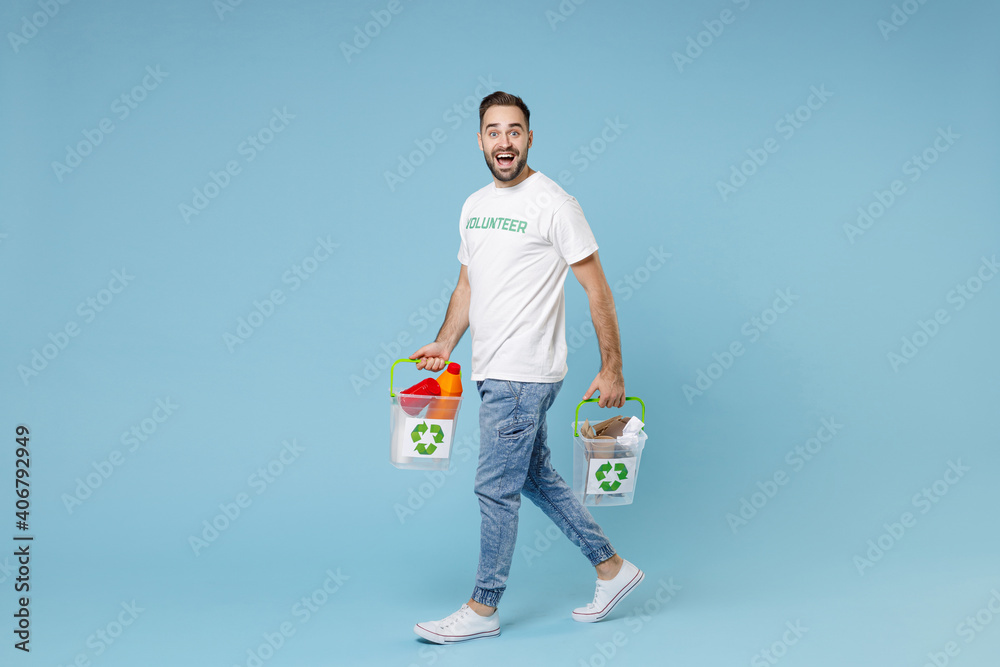 Full length of excited young man in volunteer t-shirt hold baskets with plastic paper trash isolated on blue background studio portrait. Voluntary free assistance help trash sorting recycling concept. Full length of excited young man in volunteer t-shirt hold baskets with plastic paper trash isolated on blue background studio portrait. Voluntary free assistance help trash sorting recycling concept.