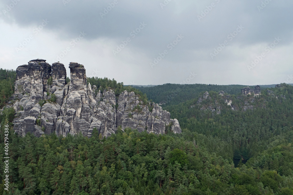 Huge black grey colored and fissured sandstone rock formations surrounded by green forest; Saxon Switzerland, Germany, Europe