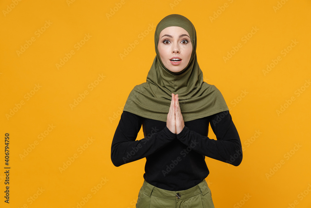 Pleading young arabian muslim woman in hijab black green clothes hold hands folded in prayer gesture, begging about something isolated on yellow background studio. People religious lifestyle concept. Pleading young arabian muslim woman in hijab black green clothes hold hands folded in prayer gesture, begging about something isolated on yellow background studio. People religious lifestyle concept.