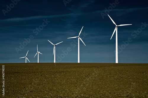 A row of windmills stand tall against a deep, dark blue sky.