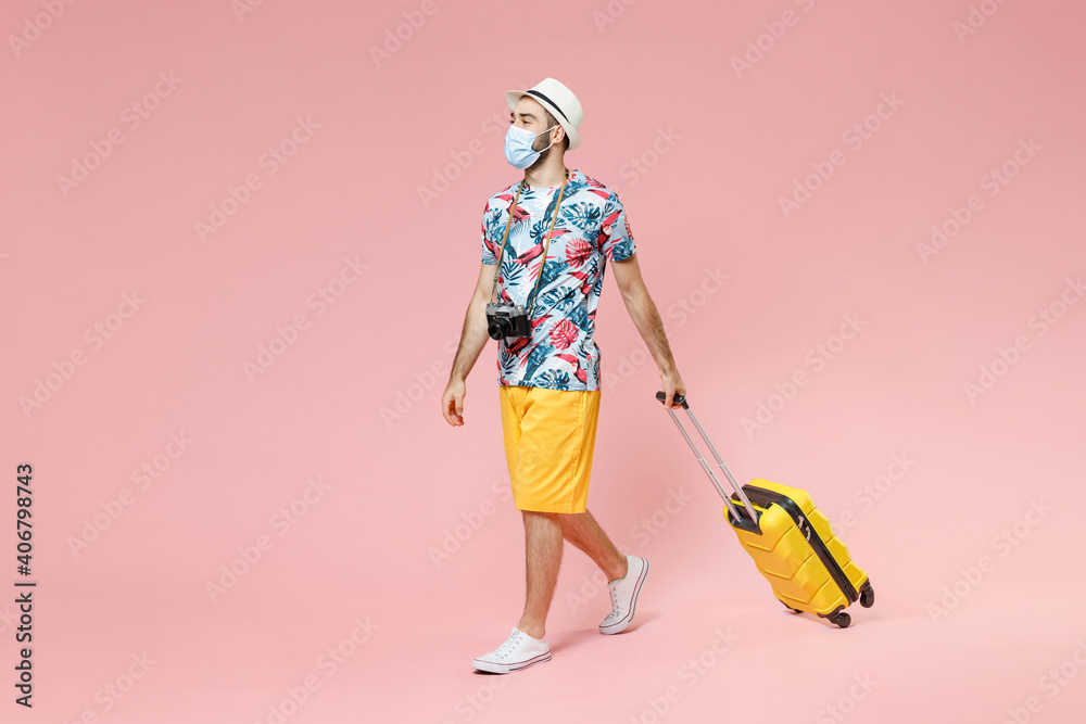 Full length young traveler tourist man in sterile face mask to safe from coronavirus covid-19 hold suitcase isolated on pink background. Passenger traveling on weekends. Air flight journey concept. Full length young traveler tourist man in sterile face mask to safe from coronavirus covid-19 hold suitcase isolated on pink background. Passenger traveling on weekends. Air flight journey concept.
