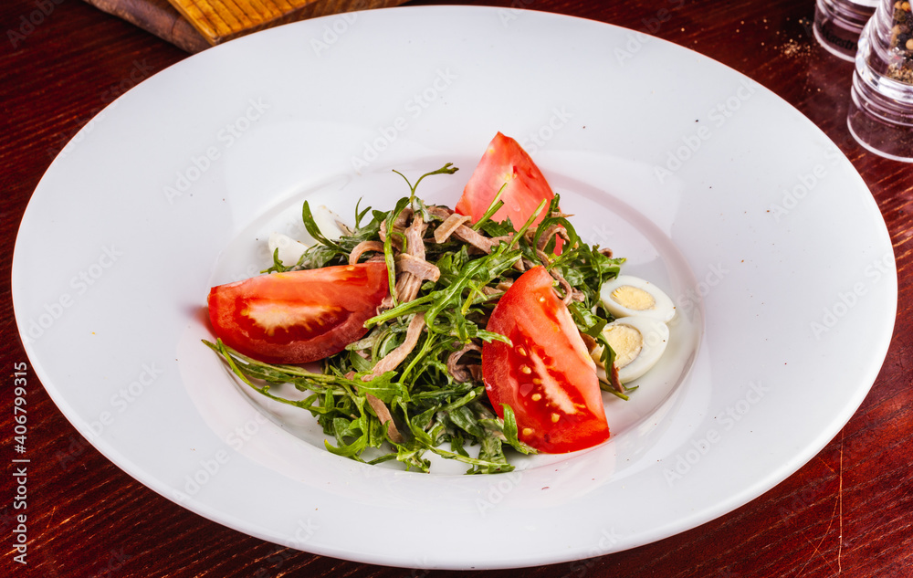 Beef tongue salad with arugula, tomatoes and quail egg on white plate