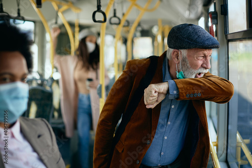 Senior man coughing into elbow while commuting by bus.