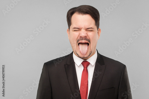 Closeup portrait of crazy man in classic suit, tongue out, and roar. indoor studio shot. isolated on gray background. handsome businessman with black suit, red tie and mustache with closed eyes