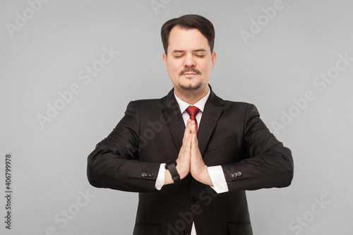 During a work break, it is best to do yoga to put your nerves in order. indoor studio shot. isolated on gray background. handsome businessman with black suit, red tie and mustache.