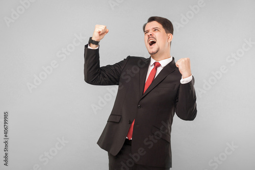 Businessman rejoicing won the jackpot in the lottery. indoor studio shot. isolated on gray background. handsome businessman with black suit, red tie and mustache looking away.