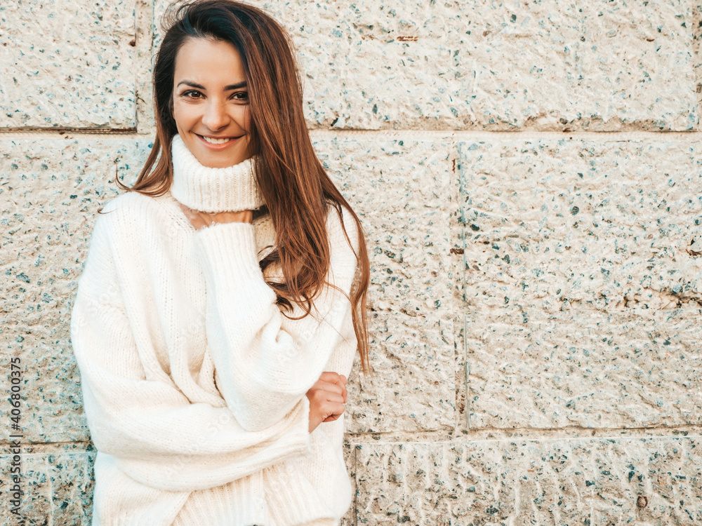 Portrait of beautiful smiling model. Female dressed in warm hipster white sweater. Posing near wall in the street. Funny and positive woman having fun outdoors Portrait of beautiful smiling model. Female dressed in warm hipster white sweater. Posing near wall in the street. Funny and positive woman having fun outdoors