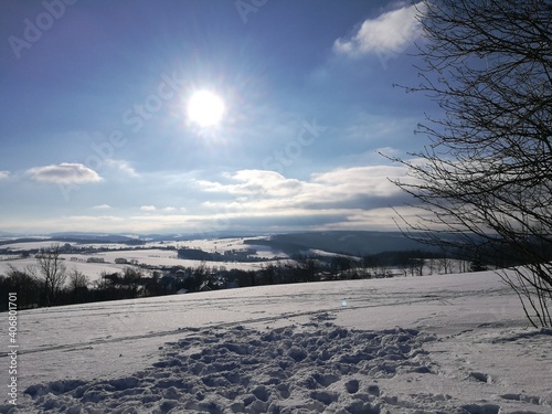 Skispuren in einer Winterlandschaft; hügelige Landschaft im Erzgebirge in Sachsen, Wintersonne am blauen Himmel, 