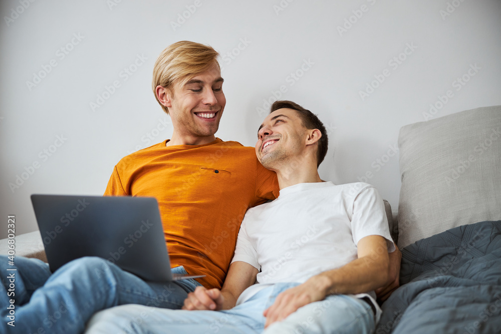 Happy gay couple cuddling and using laptop at home Happy gay couple cuddling and using laptop at home