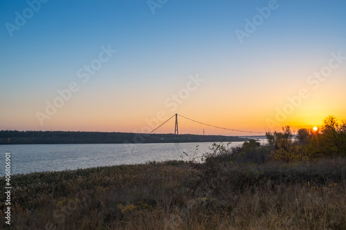 Beautiful landscape. Cable-stayed bridge over the Dnieper river against the backdrop of a beautiful orange setting sun © okrip