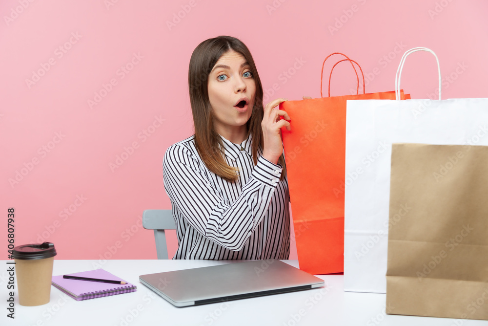 Surprised brunette woman employee touching paper bags looking at camera with big eyes and open mouth, shocked with easy shopping online. Indoor studio shot isolated on pink background Surprised brunette woman employee touching paper bags looking at camera with big eyes and open mouth, shocked with easy shopping online. Indoor studio shot isolated on pink background
