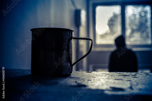a metal mug stands on a concrete staircase stands, in the background a homeless man