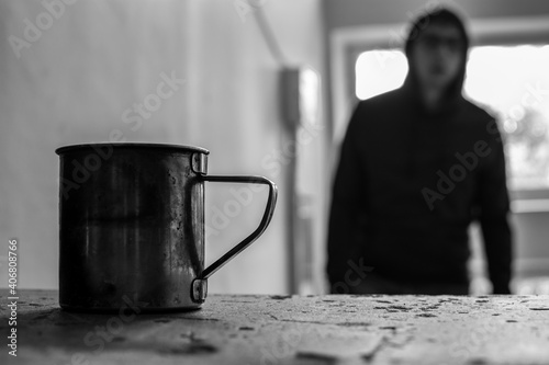 a metal mug stands on a concrete staircase stands, in the background a homeless man
