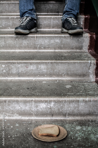 A paper plate of bread stands on a concrete staircase stands, in the background a homeless man