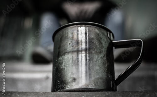a metal mug stands on a concrete staircase stands, in the background a homeless man