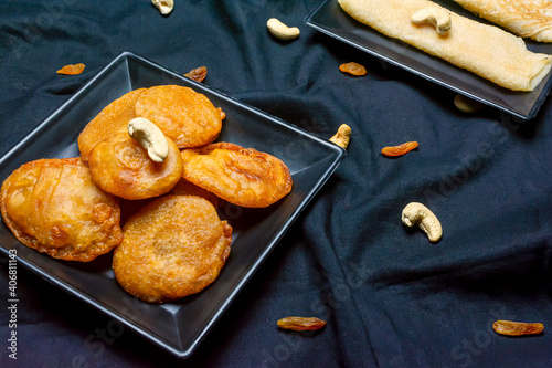 Bengali sweet - Patishapta Pitha and Malpua in a black plate on black cloth texture background with cashew nut and raisins. photo
