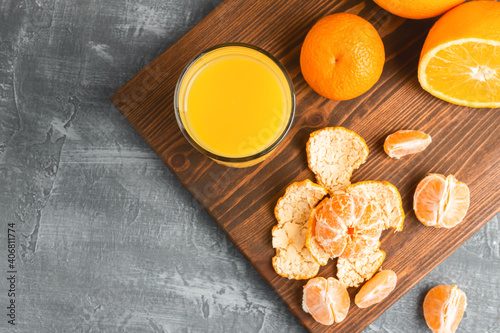 Glass of fresh orange juice, whole and sliced fruits on wooden board, top view with copy-space