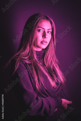 Portrait of young Caucasian model illuminated with pink neon lights. On a black wall background