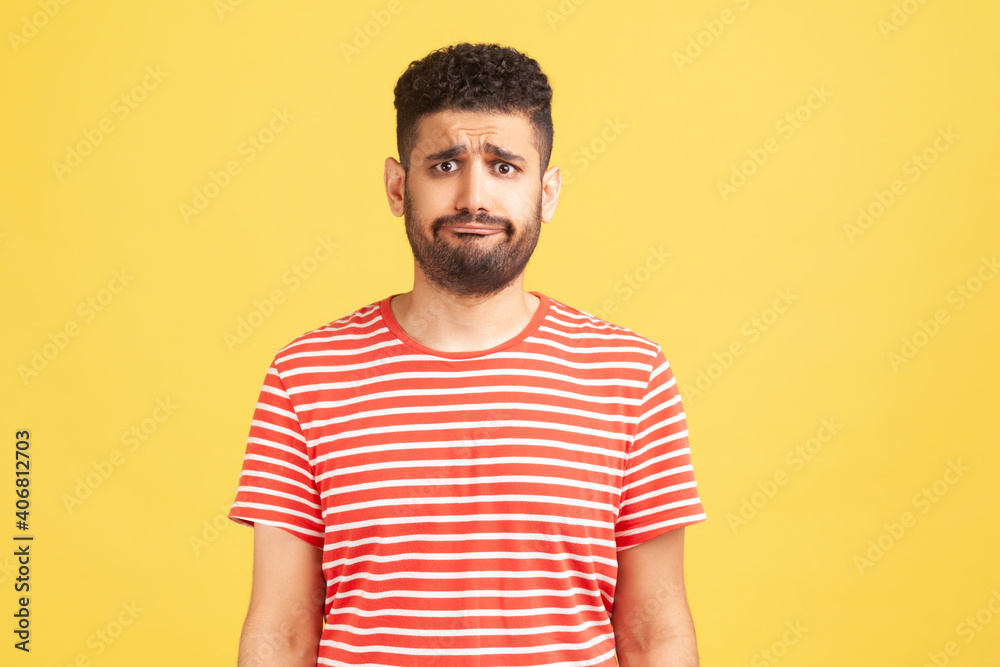 Frustrated unhappy man with beard in striped t-shirt looking at camera with sad dissatisfied expression, bad mood. Indoor studio shot isolated on yellow background Frustrated unhappy man with beard in striped t-shirt looking at camera with sad dissatisfied expression, bad mood. Indoor studio shot isolated on yellow background