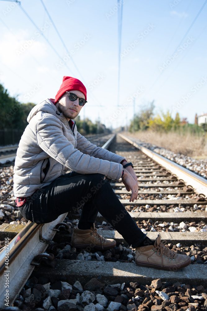 Pretty caucasian male model sits on the train track on a winter day. He wears sunglasses and he is thoughtful and worried about the future
Pretty caucasian male model sits on the train track on a winter day. He wears sunglasses and he is thoughtful and worried about the future