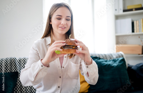 Young woman with take away hamburger at home  coronavirus and food delivery concept.