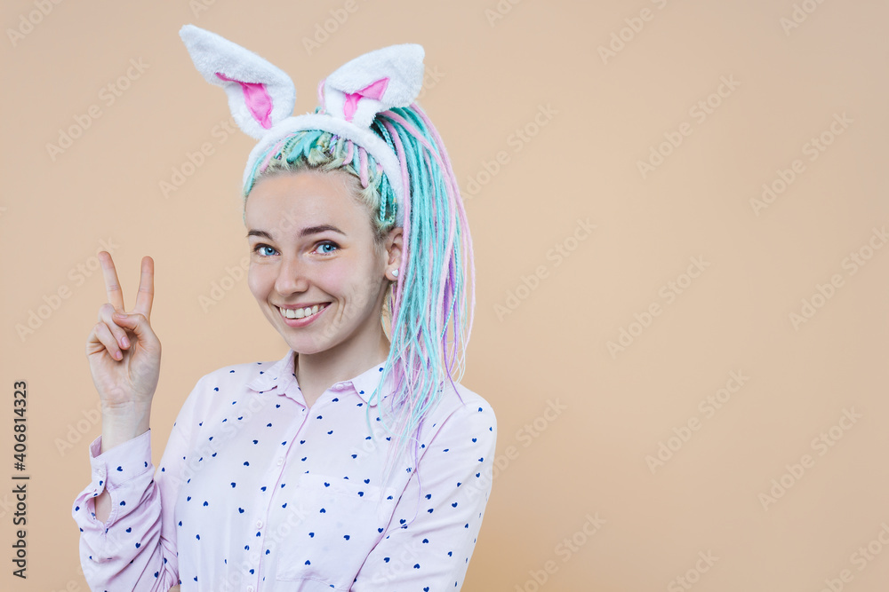 Pretty cute girl in bunny ears, pink shirt is smiling. Young woman with colored dreadlocks is preparing for celebration. Happy easter, spring concept. Carnival, seasonal party decor for holiday.