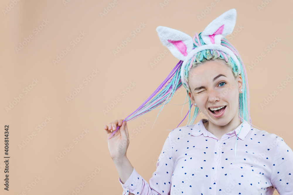 Pretty cute girl in bunny ears, pink shirt is winking. Young woman with colored dreadlocks is preparing for celebration. Happy easter, spring concept. Carnival, seasonal party decor for holiday. Pretty cute girl in bunny ears, pink shirt is winking. Young woman with colored dreadlocks is preparing for celebration. Happy easter, spring concept. Carnival, seasonal party decor for holiday.