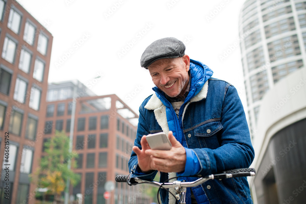Happy senior man with bicycle outdoors on street in city, using smartphone.
